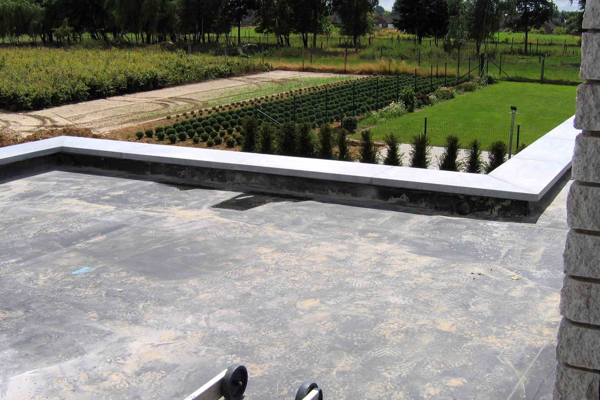 Een afgewerkt plat dak in EPDM met een lichte dakrand, tuin op de achtergrond