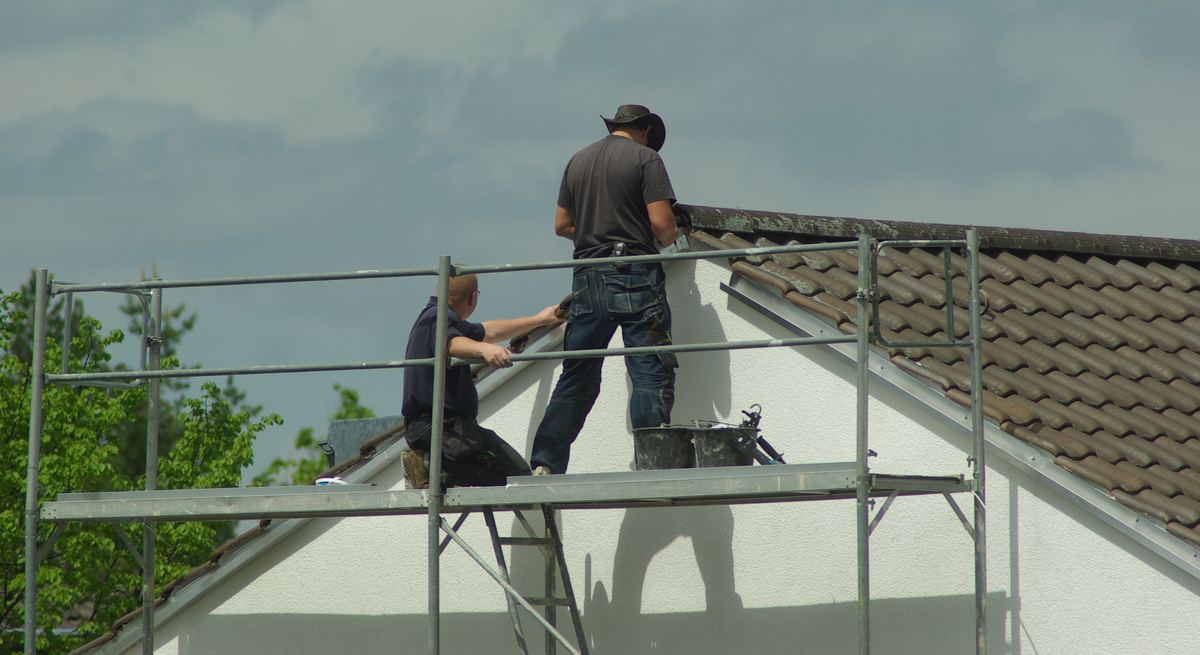 Twee dakwerkers op een stelling werken aan de rand van een pannendak