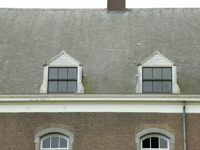 Een leien dak met twee kleine dakkapellen boven een bakstenen gevel